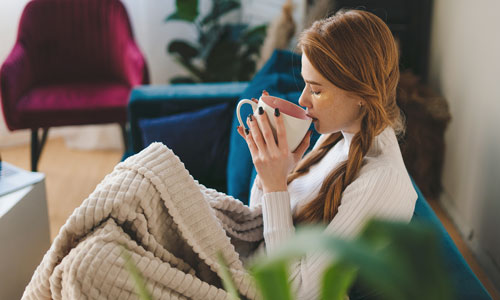Woman Cosy On Sofa With Blanket & Hot Drink